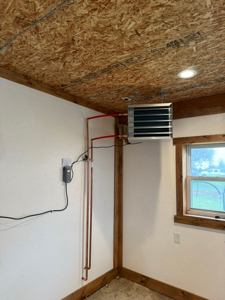 Small room corner with wall-mounted heater, exposed copper pipes, window, and wood-paneled ceiling