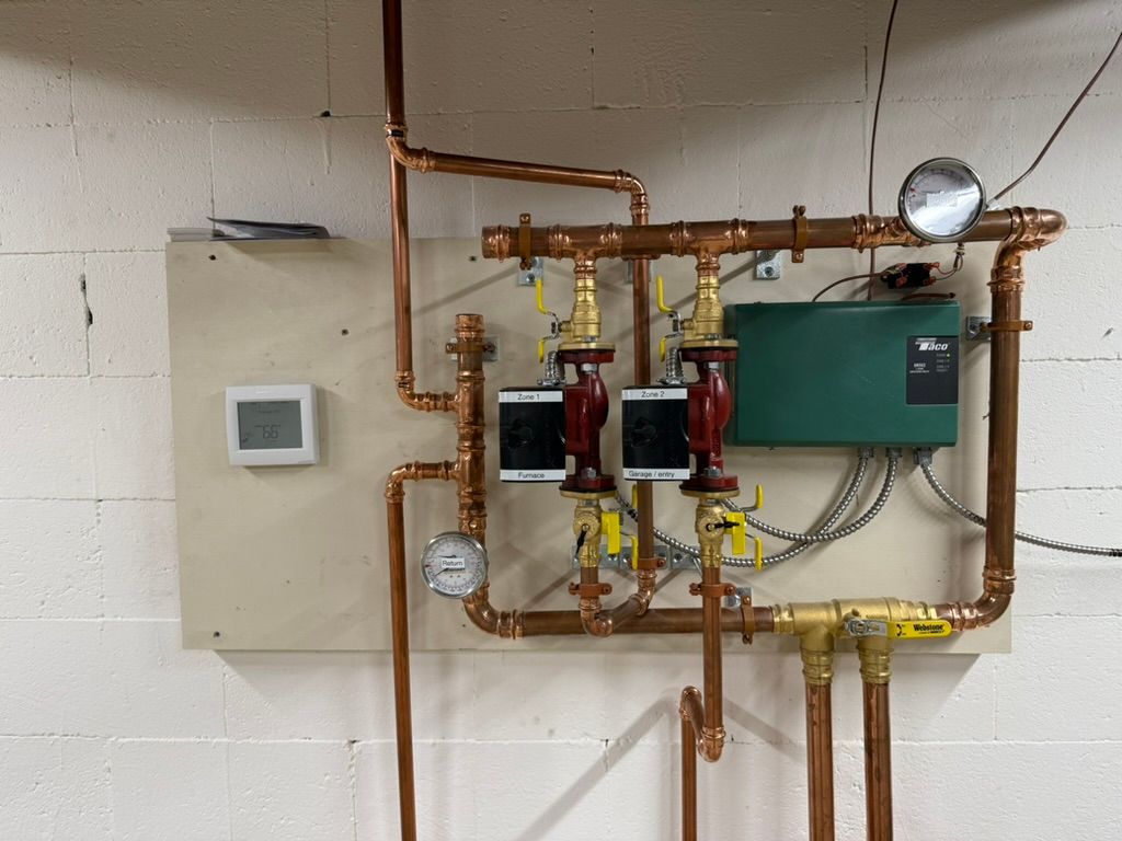 Mechanical room with copper pipes, gauges, pumps, and a wall thermostat/controller.