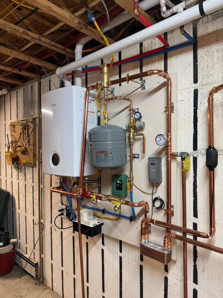 Basement wall with water heater, boiler, copper pipes, and utility meters under exposed ceiling beams
