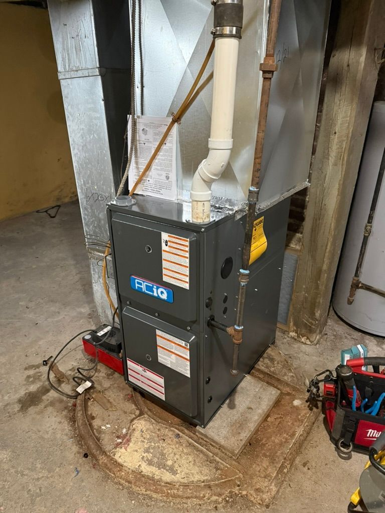 Gray furnace unit in a basement utility area, with metal ductwork and pipes around it.