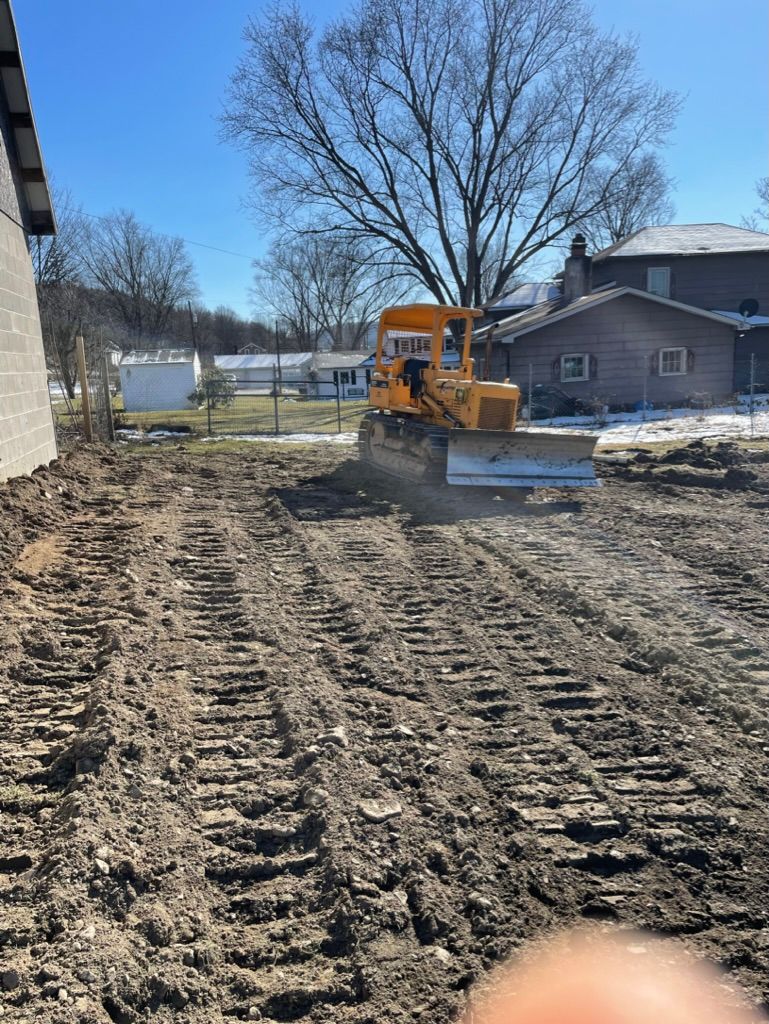 Yellow skid steer smoothing dirt in a backyard beside a house on a sunny day