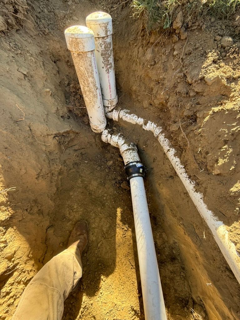 Underground PVC pipes connected by a black elbow joint in a dirt trench