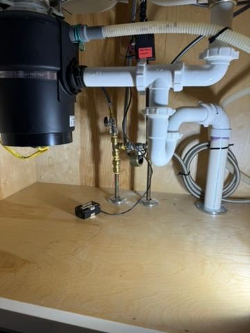Under-sink plumbing with white PVC pipes, valves, and a black garbage disposal inside a cabinet