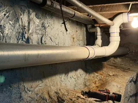 Basement with exposed pipes and a red power tool on the dirt floor