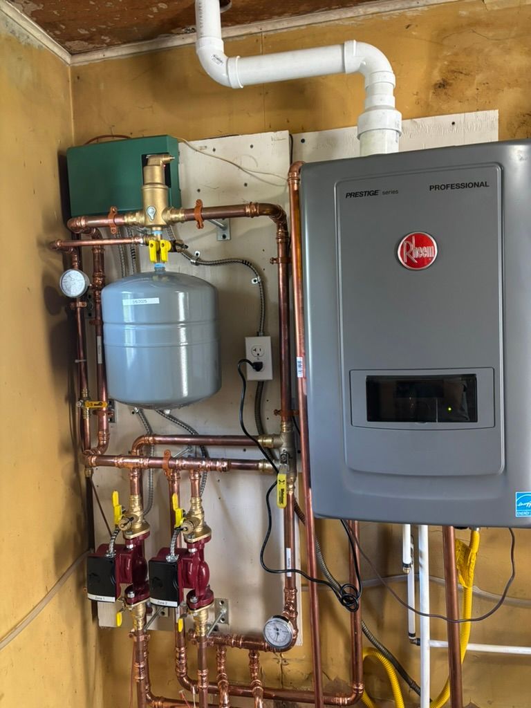 Wall-mounted water heater and plumbing manifold in a utility room, with gray tank and control unit.