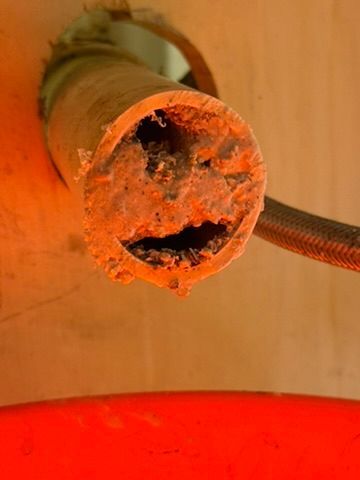 Close-up of a rusted, corroded metal pipe opening with orange residue and a red container below