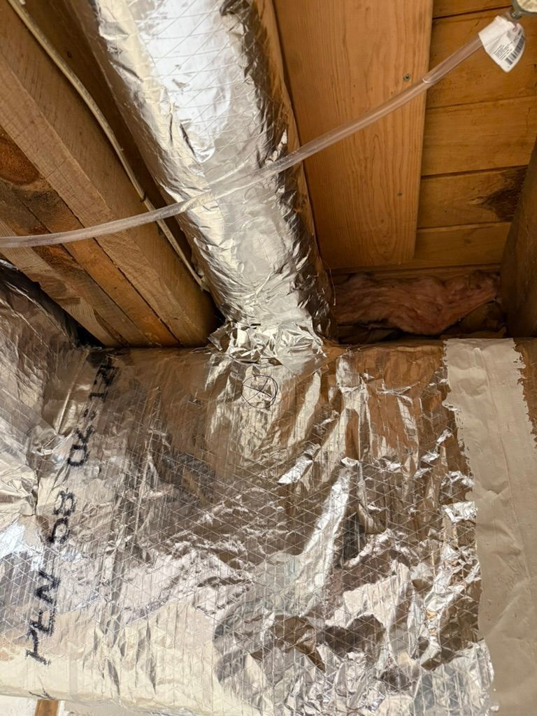 Insulated attic corner with exposed wooden beams and foil-faced vapor barrier