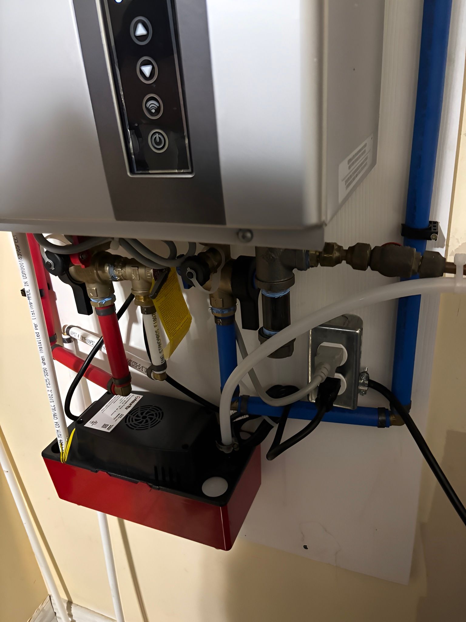 Boiler or water heater with exposed pipes, cables, and a red pump unit in a utility room.