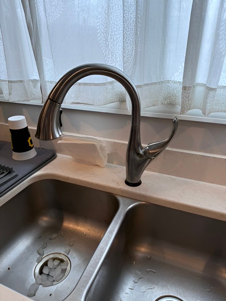 Kitchen sink with stainless steel faucet, double basins, and a soap dispenser by a window curtain.