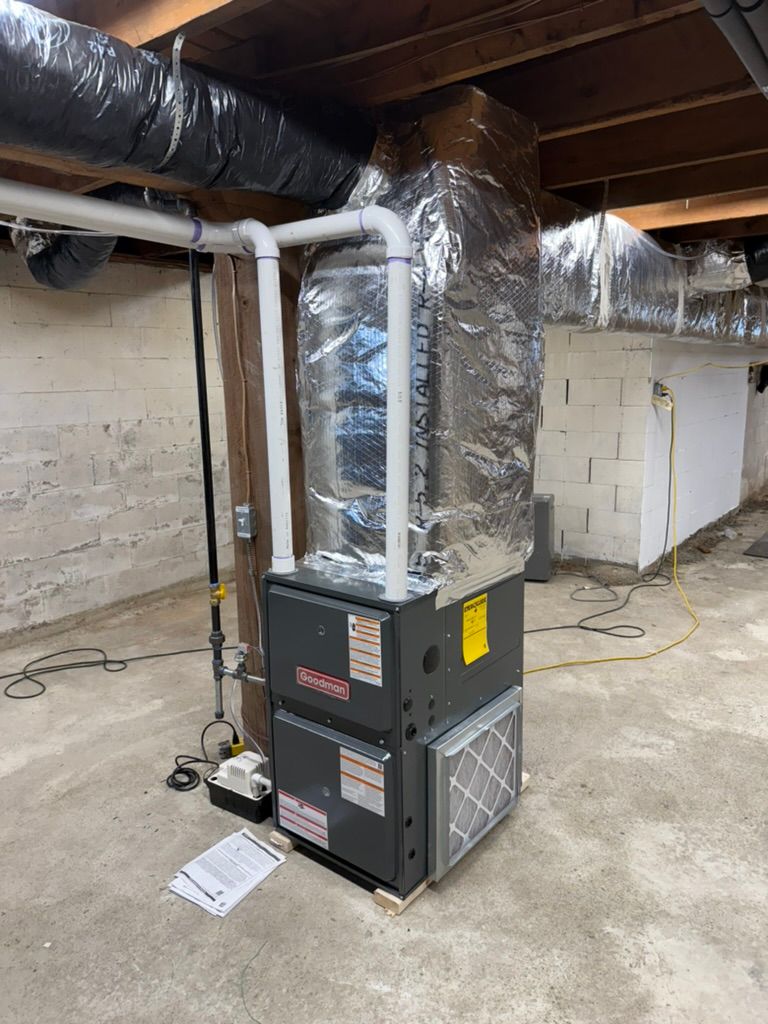 Basement utility room with a gray HVAC furnace and silver ductwork under exposed ceiling beams.