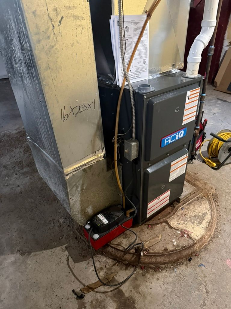 Furnace unit in a basement beside ductwork, with tools and a red floor pump nearby.