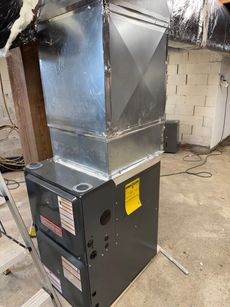 Large metal HVAC furnace with ductwork in a basement utility room