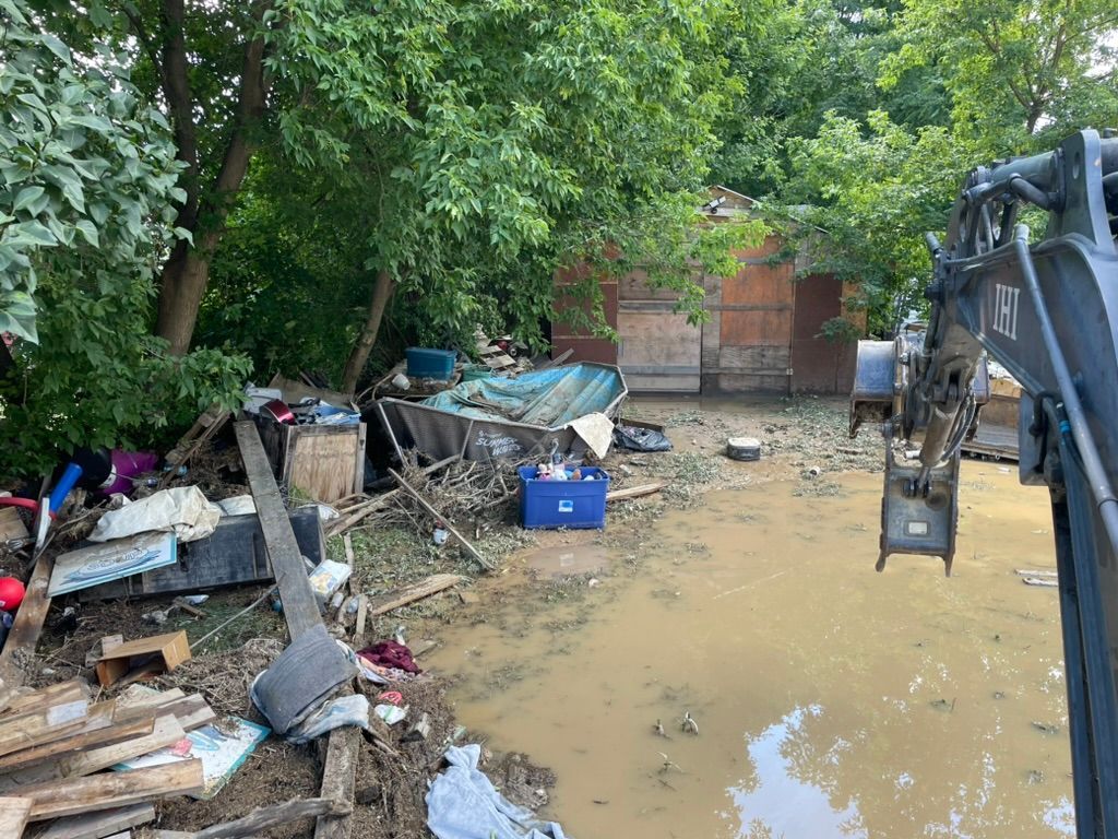 Flooded backyard with muddy water, scattered debris, and trees along a brick wall