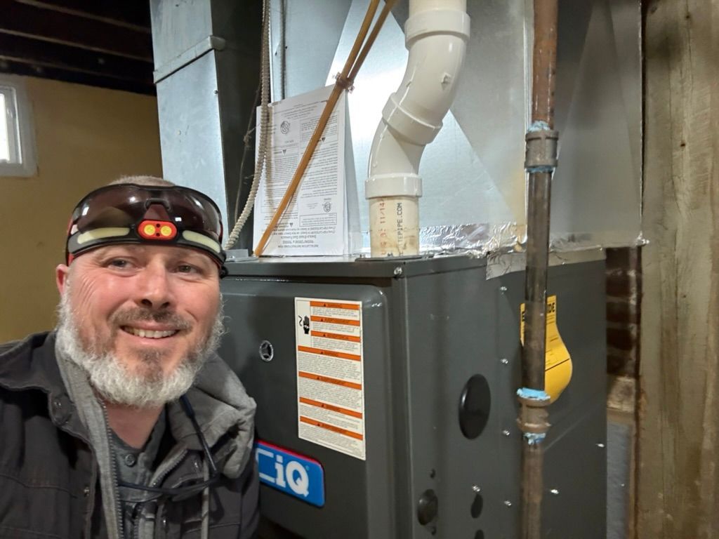 Smiling man in headlamp selfie beside HVAC unit and ductwork in a utility room