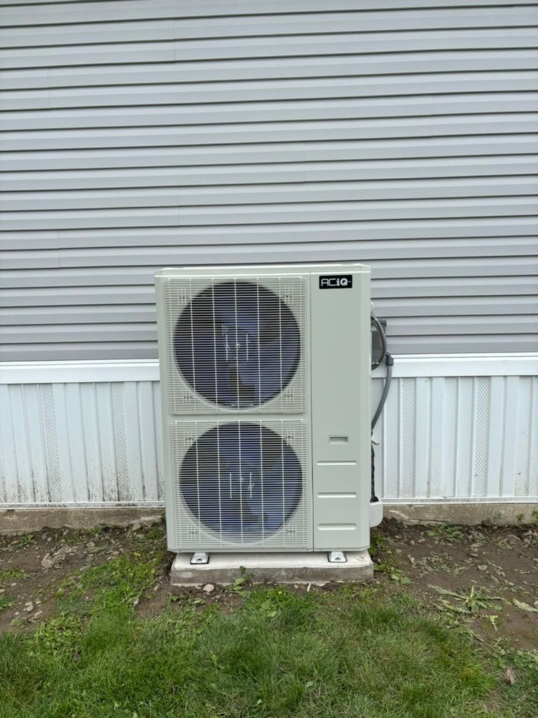 Outdoor heat pump unit against a gray wall with grass in front