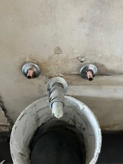 Dirty wall-mounted sink with two faucets and a central drain pipe.