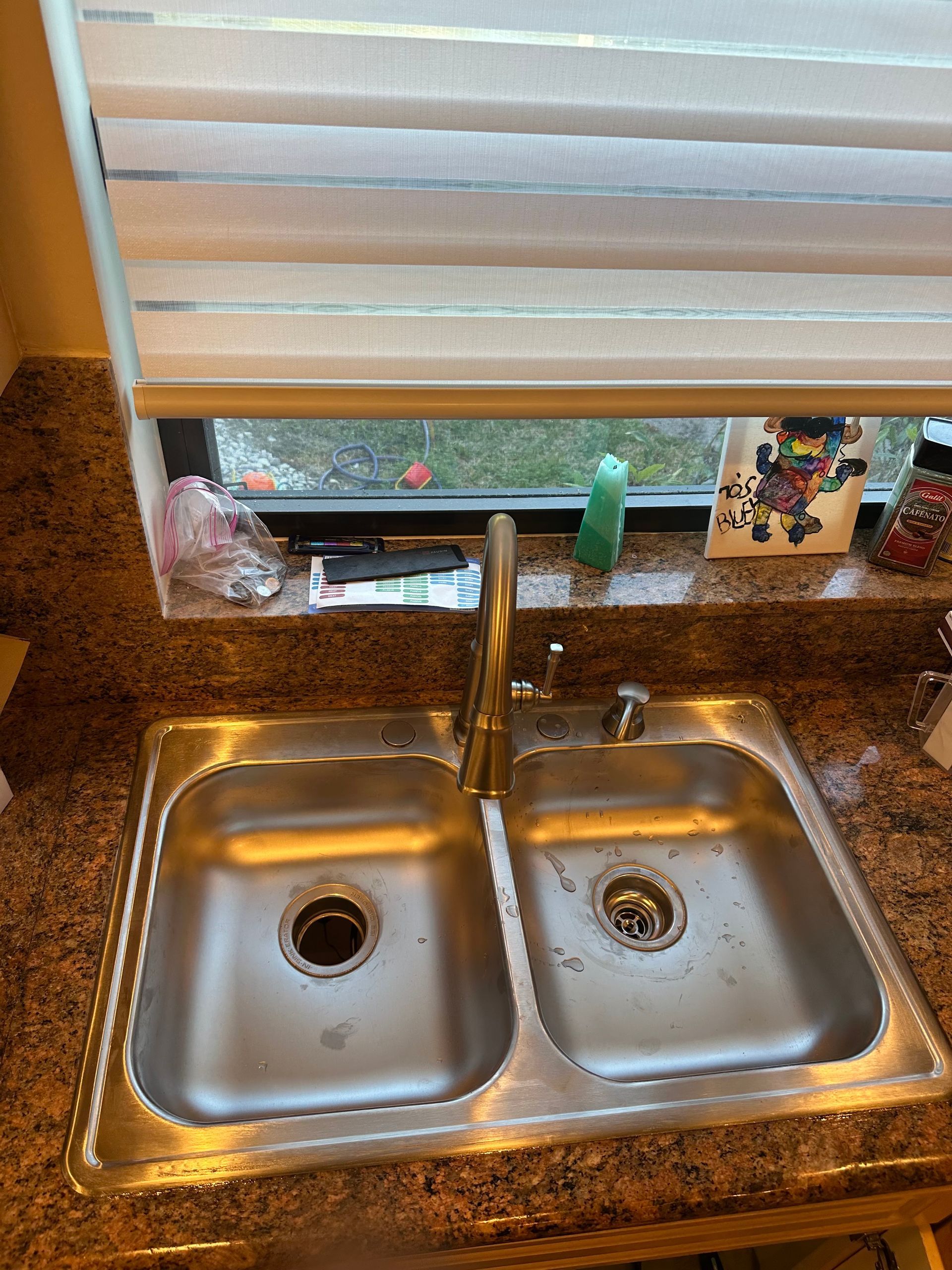 Double kitchen sink with granite countertop beneath a window and closed blinds.