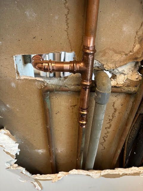Broken drywall exposing copper and gray plumbing pipes inside a wall