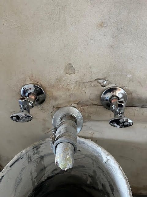 A dirty sink with two chrome faucet handles and a central spout against a stained wall.