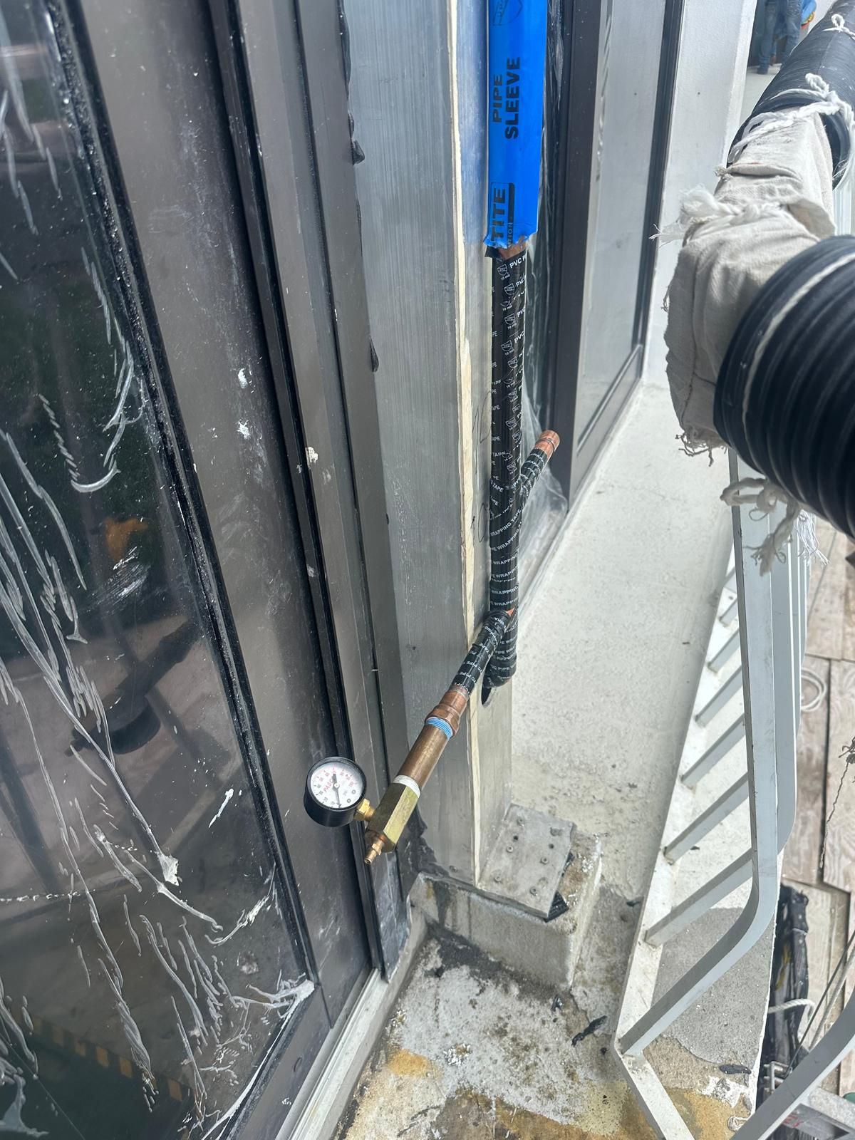 Black door edge with a blue handle and cable lock beside a concrete wall outdoors