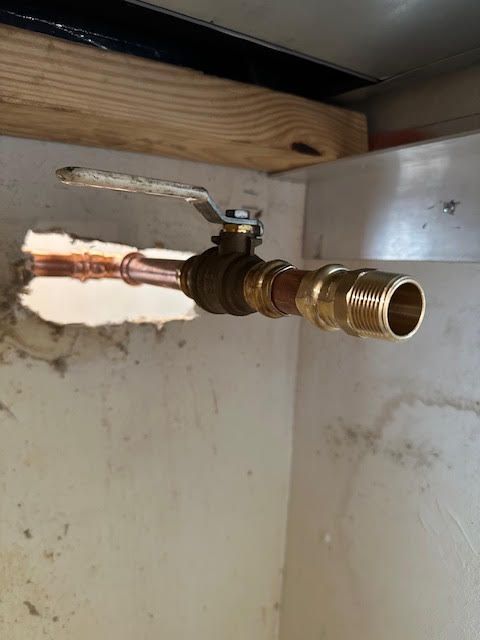 Brass shutoff valve protruding through a wall opening beneath wooden framing