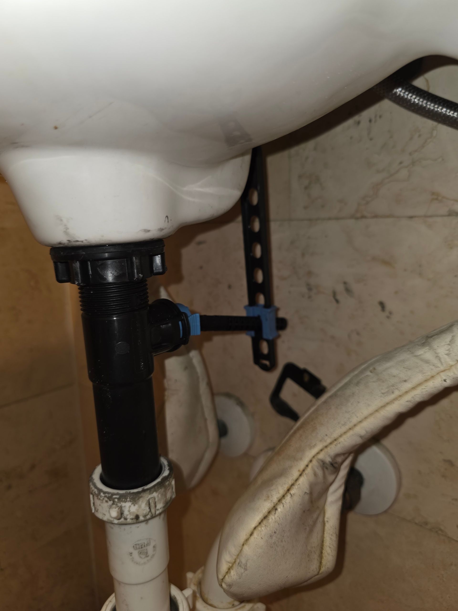 Under-sink plumbing with black and white pipes and a blue shutoff valve near a tiled wall