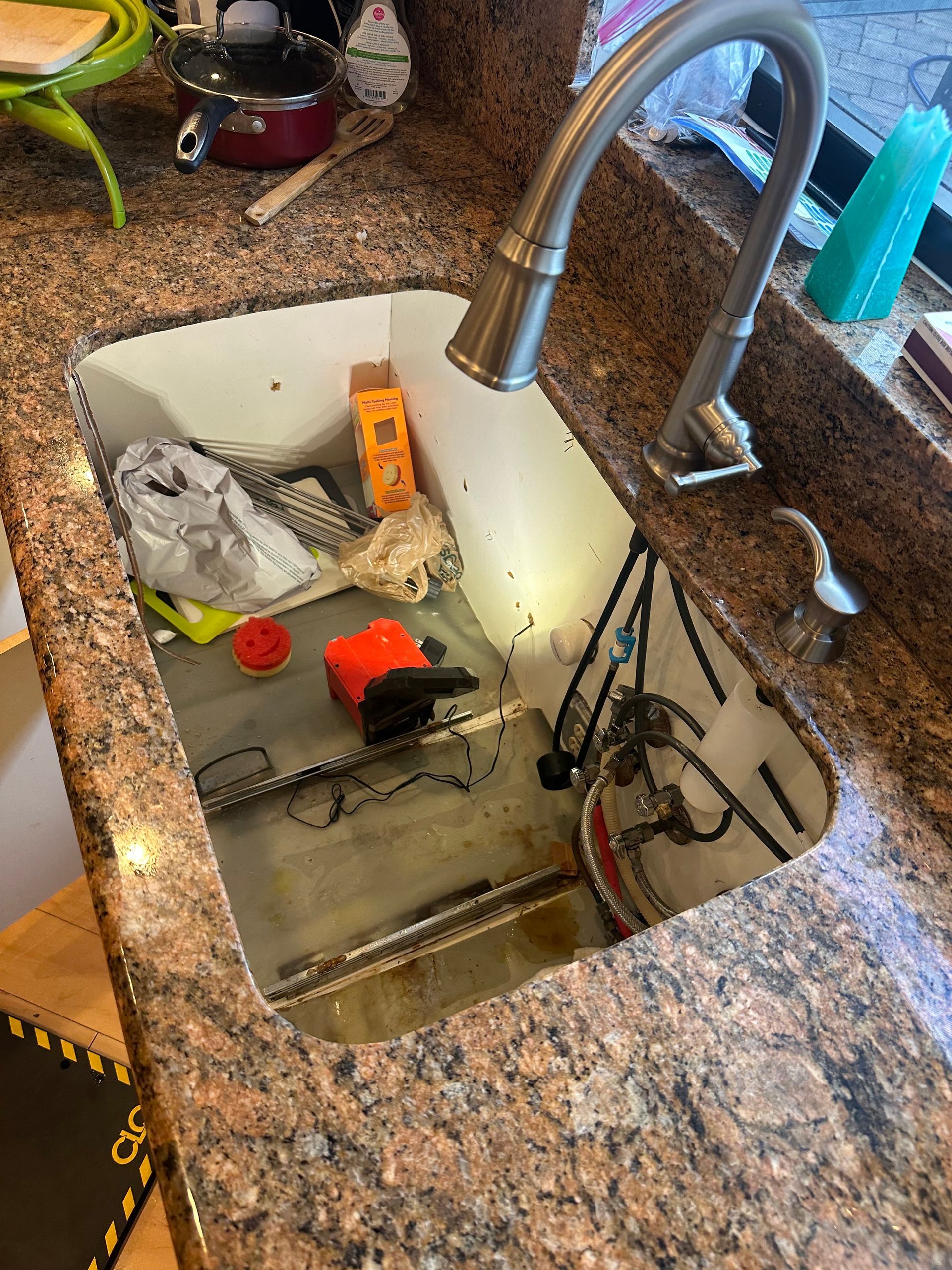 Kitchen sink full of water with cleaning supplies and utensils in a granite countertop basin