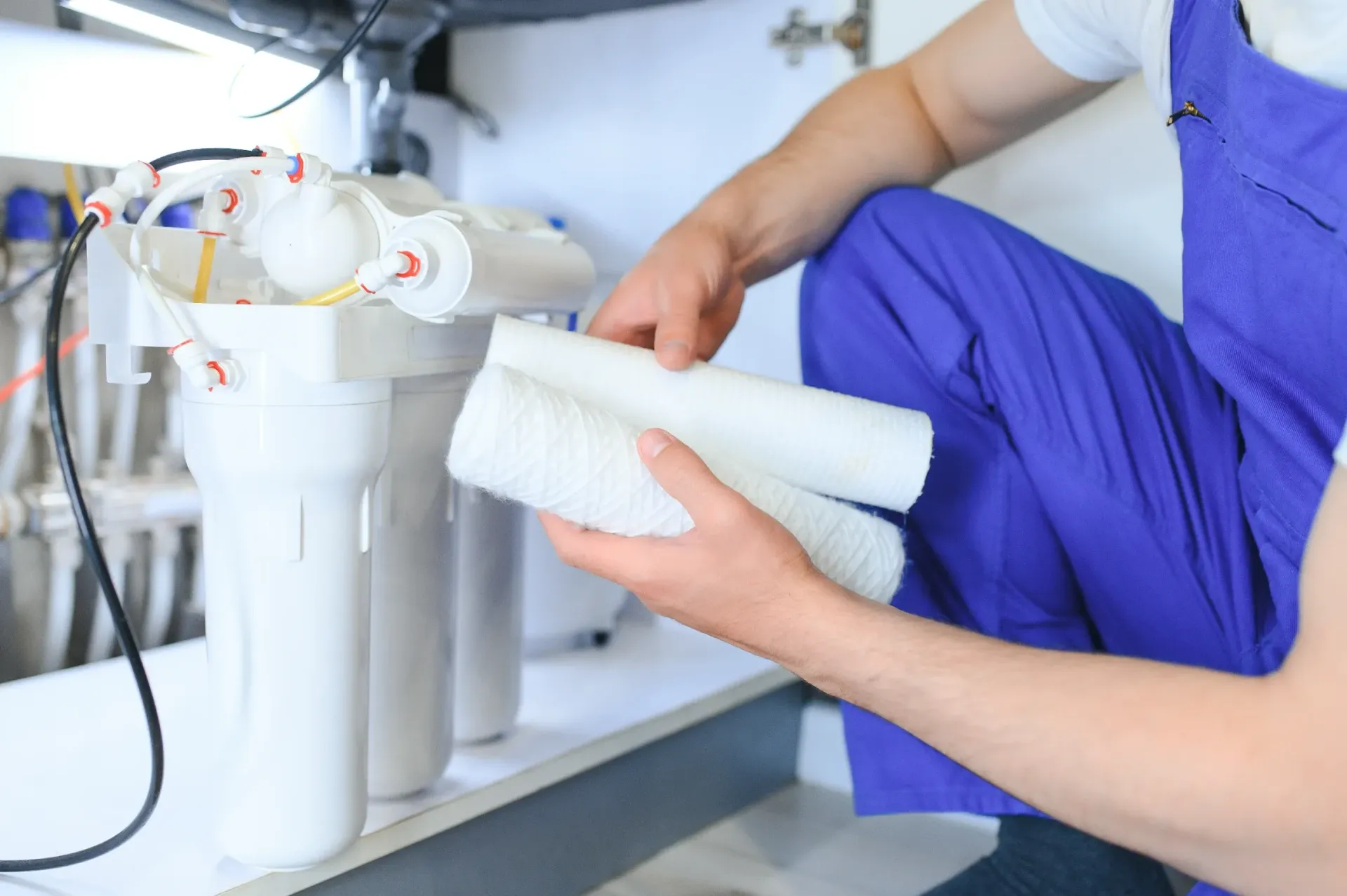 Person in blue overalls replacing water filter cartridges under a sink. — Fixtures & Fittings In Tweed Heads South, NSW