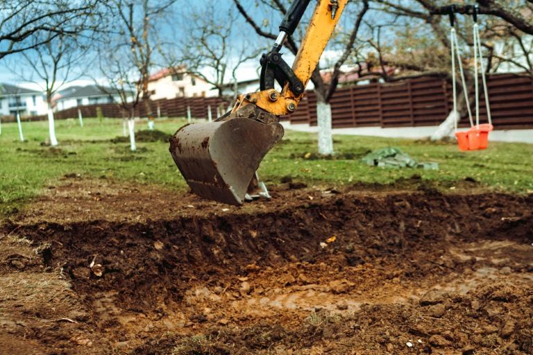 A yellow excavator is digging a hole in the ground in a yard. — Al's Excavation in Bridges, QLD