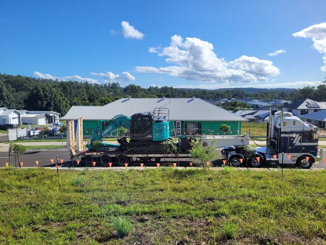 A large truck is carrying a tractor in front of a house under construction. — Al's Excavation in Bridges, QLD