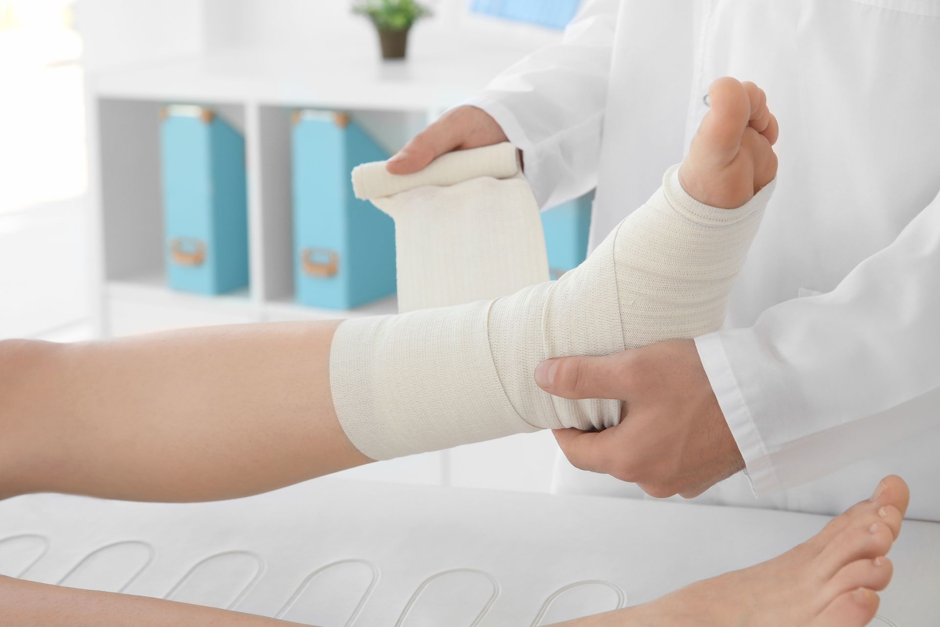 A medical professional carefully applies a bandage to a patient's injured foot.