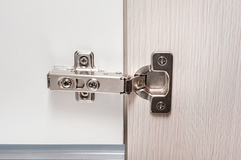 A close up of a cabinet door hinge on a wooden door.