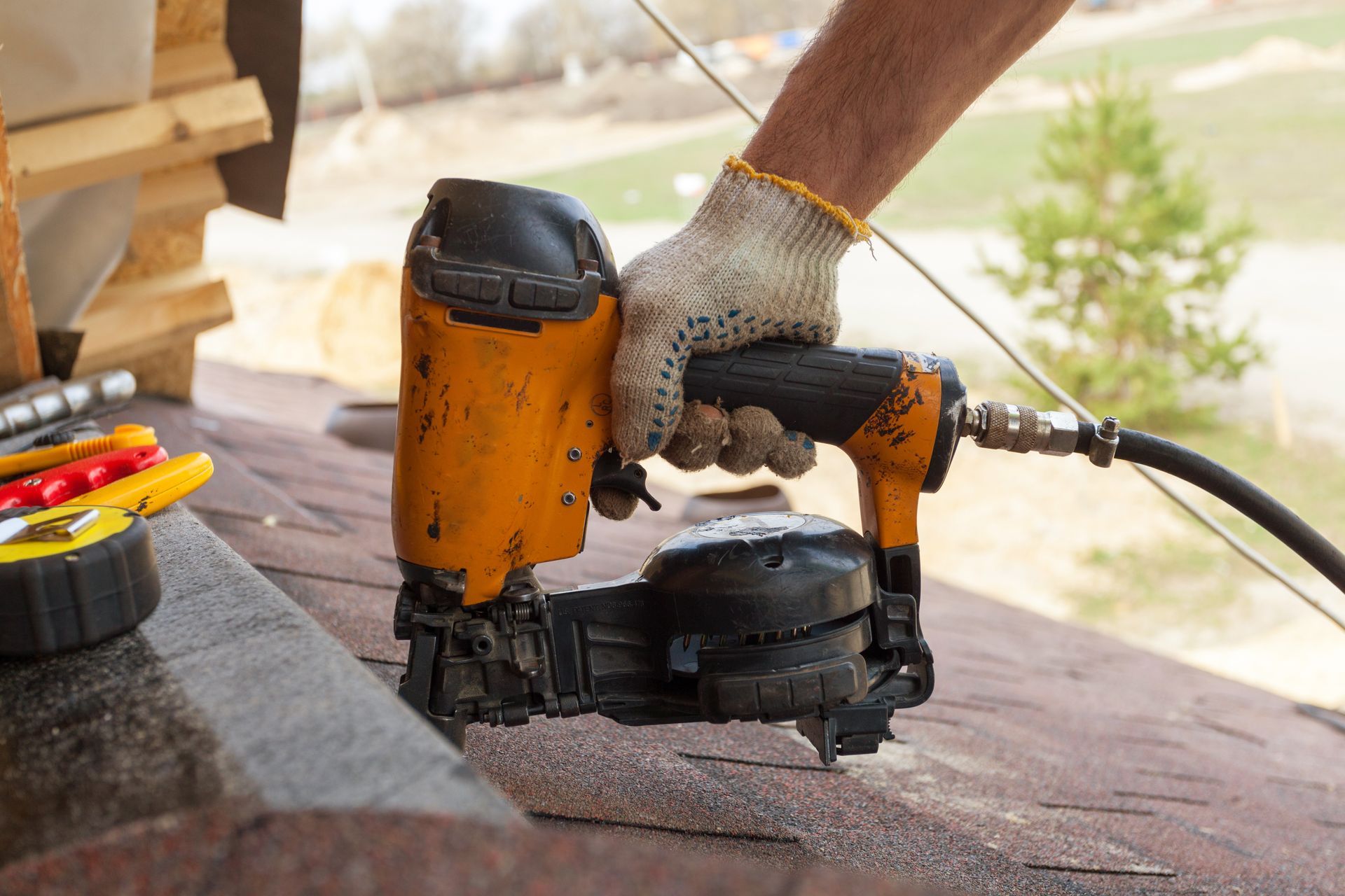 Person wearing a glove uses a pneumatic nail gun on a roof. Person wearing a glove uses a pneumatic nail gun on a roof.