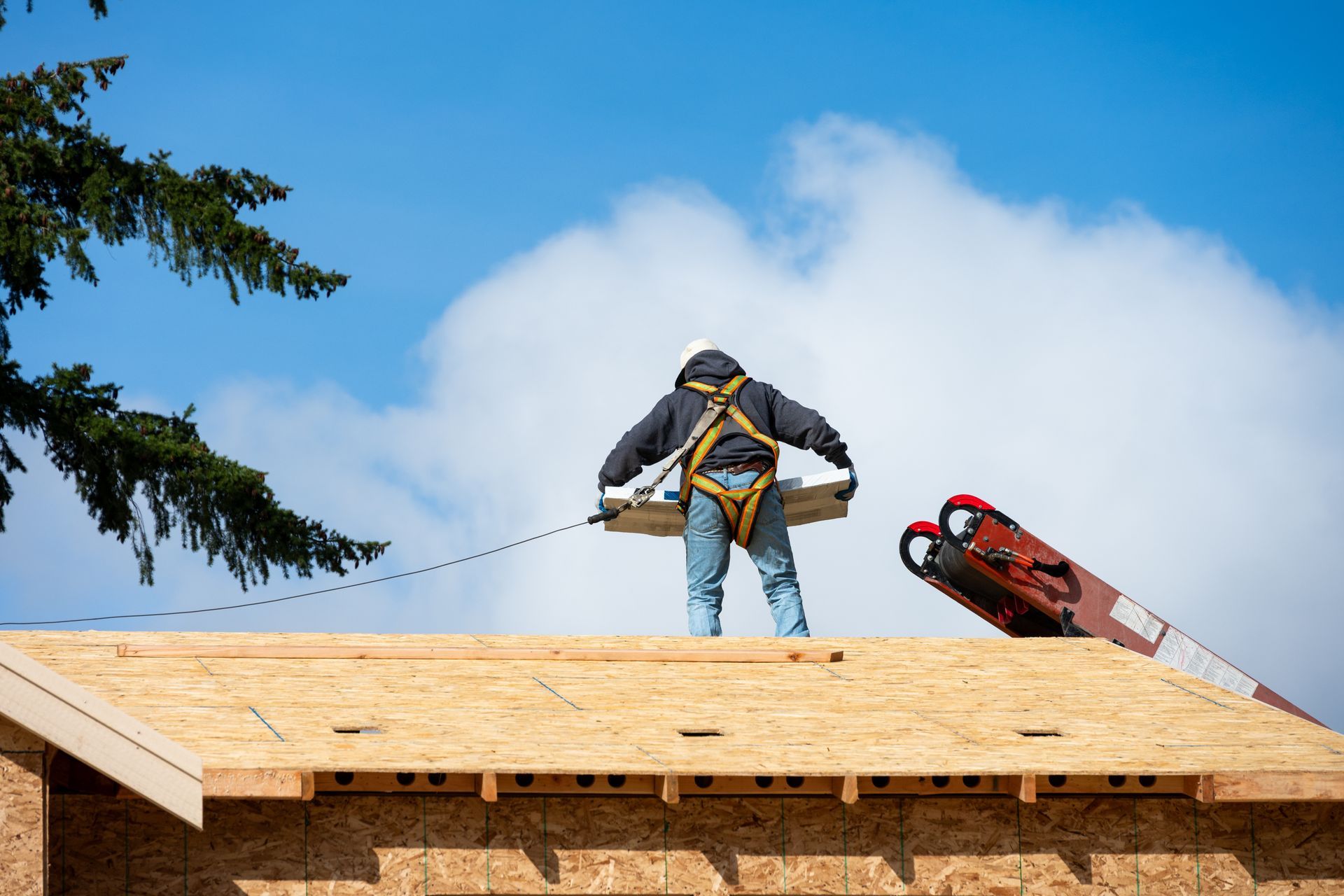 Roofer on a wood roof wearing a harness, operating a lift; blue sky with clouds. Roofer on a wood roof wearing a harness, operating a lift; blue sky with clouds.