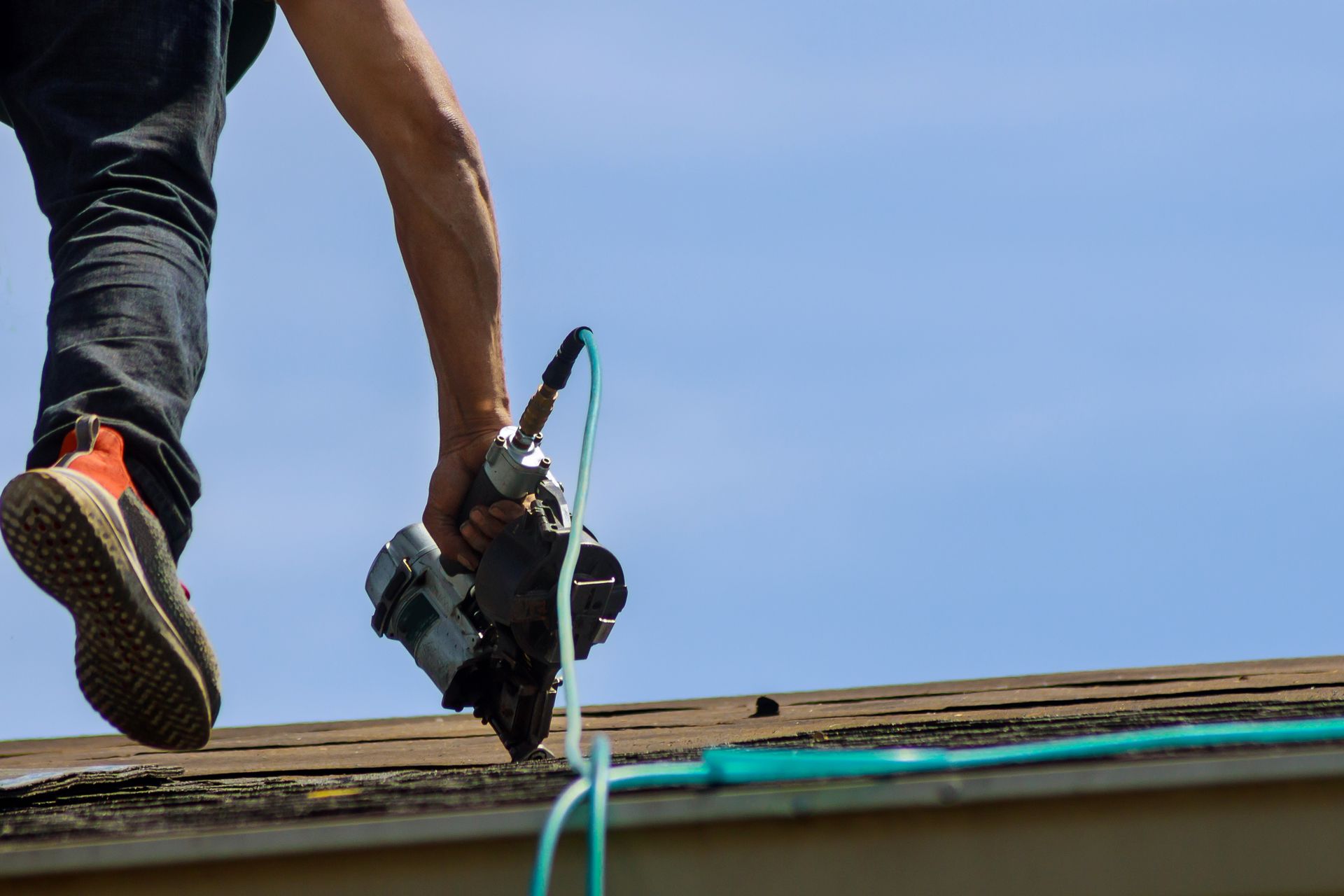 Roofer on a roof, holding a nail gun, blue sky in background. Roofer on a roof, holding a nail gun, blue sky in background.