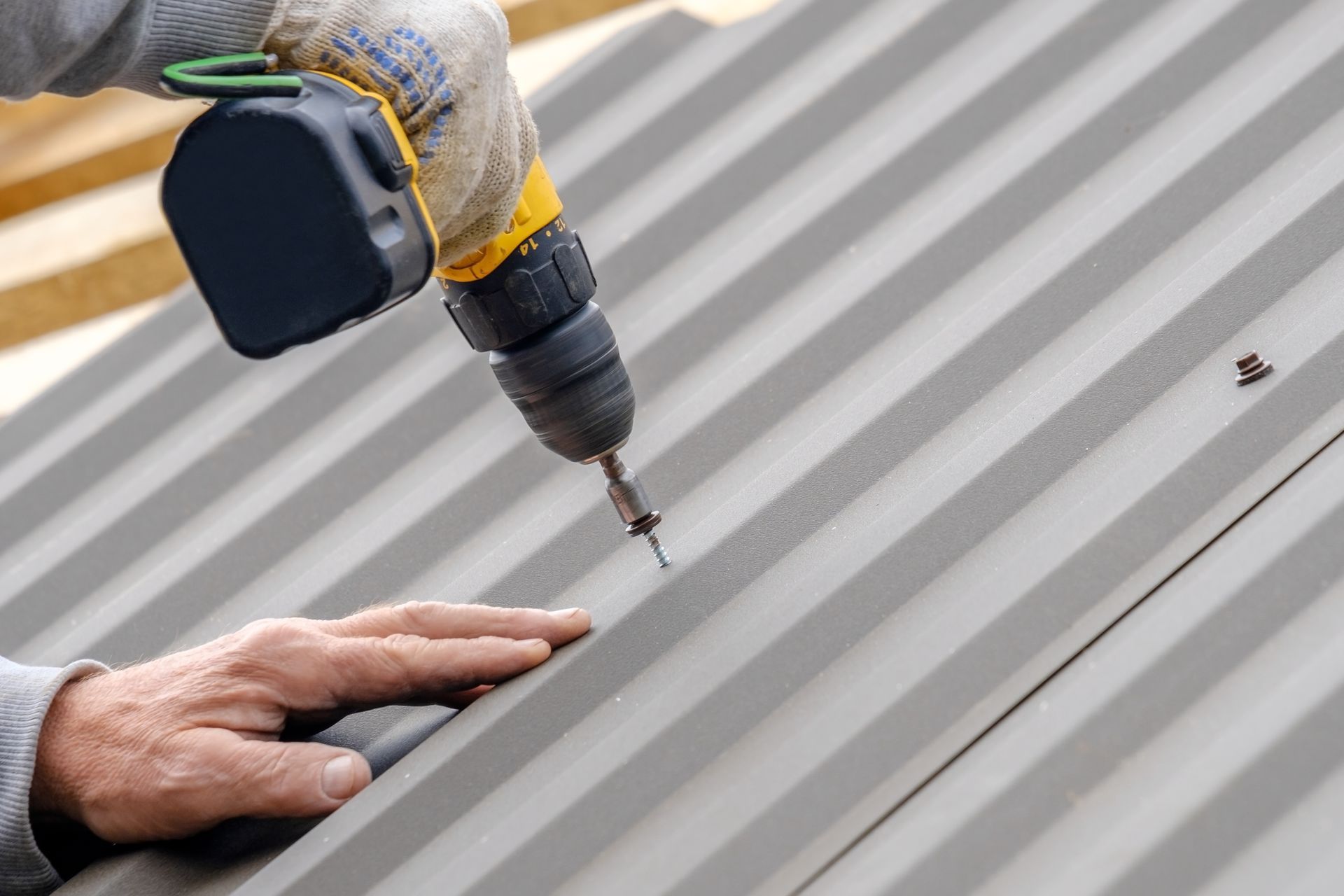 Person using a power drill to install metal roofing. Person using a power drill to install metal roofing.