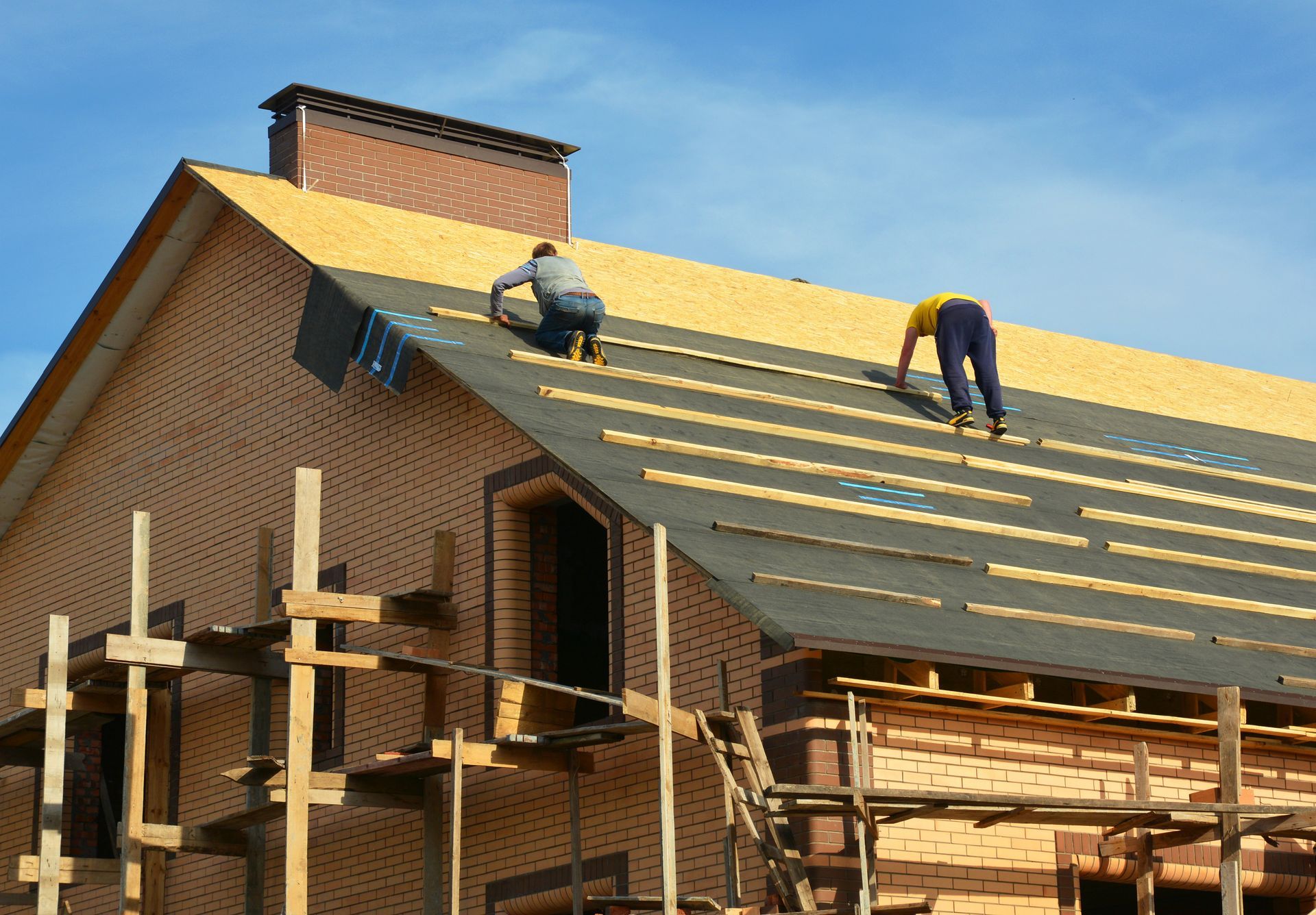 Two workers installing roof shingles on a brick house under construction. Two workers installing roof shingles on a brick house under construction.
