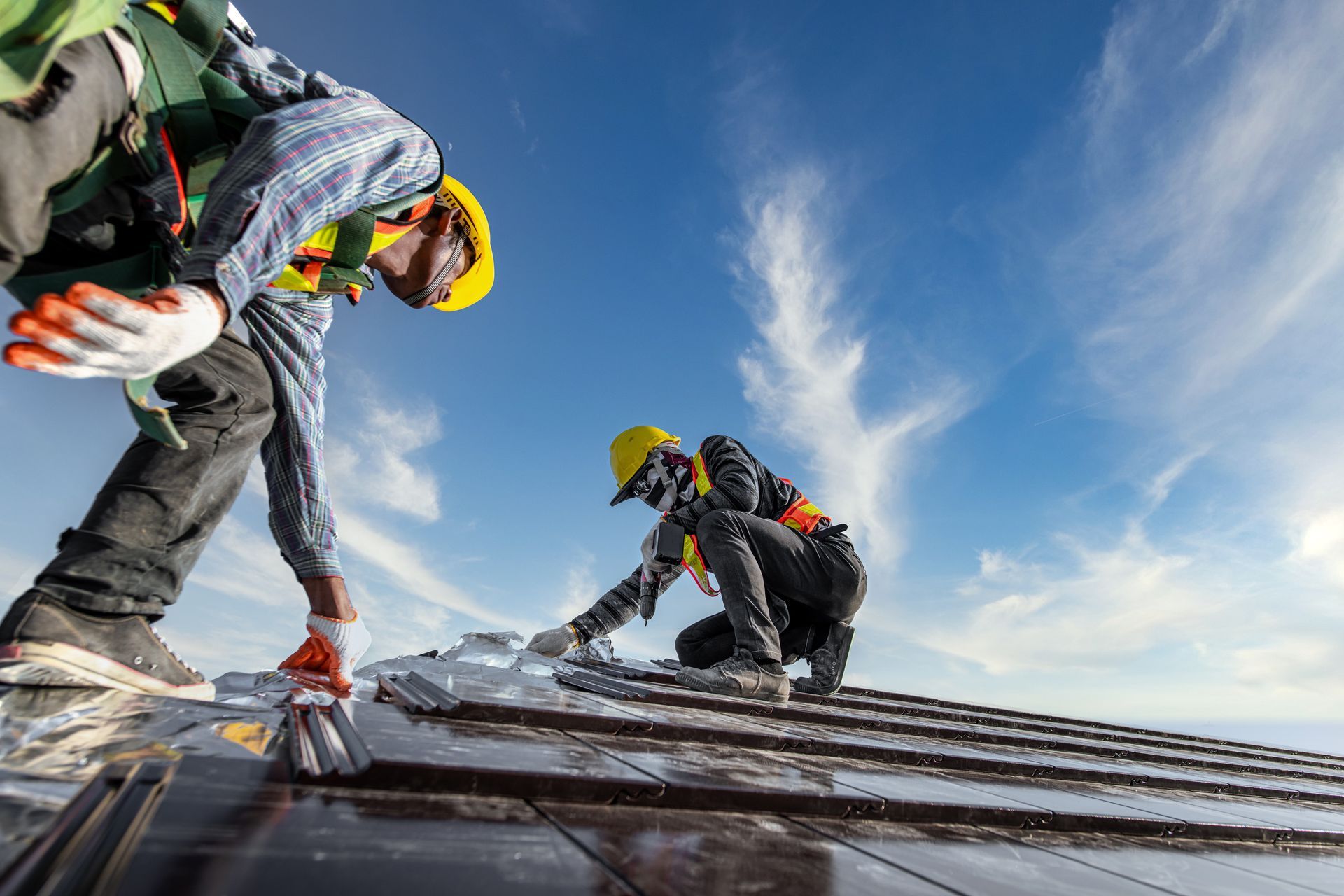 Two workers in safety gear installing solar panels on a rooftop against a blue sky. Two workers in safety gear installing solar panels on a rooftop against a blue sky.