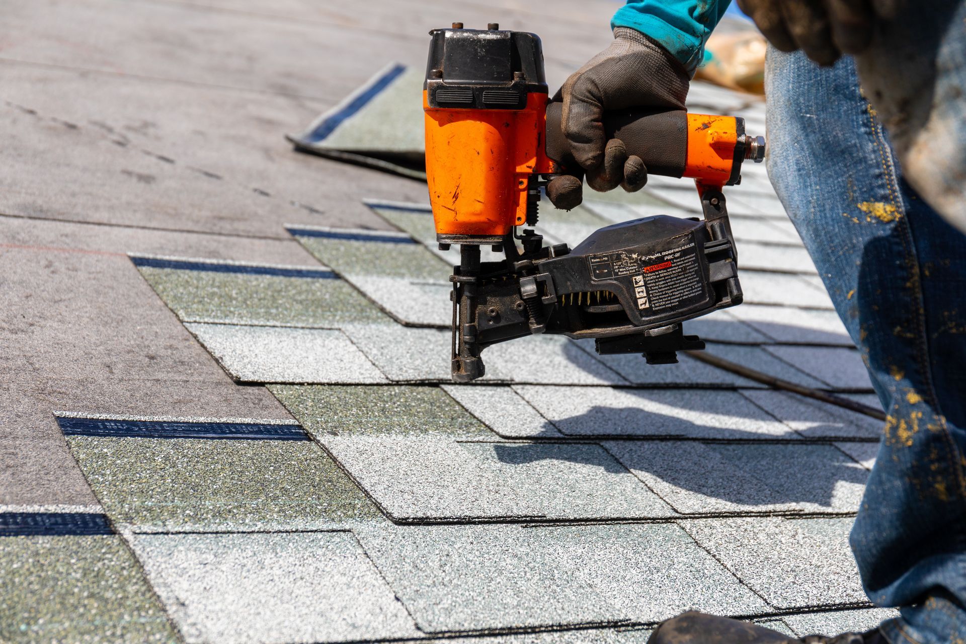 A person using a nail gun to install roofing shingles. A person using a nail gun to install roofing shingles.