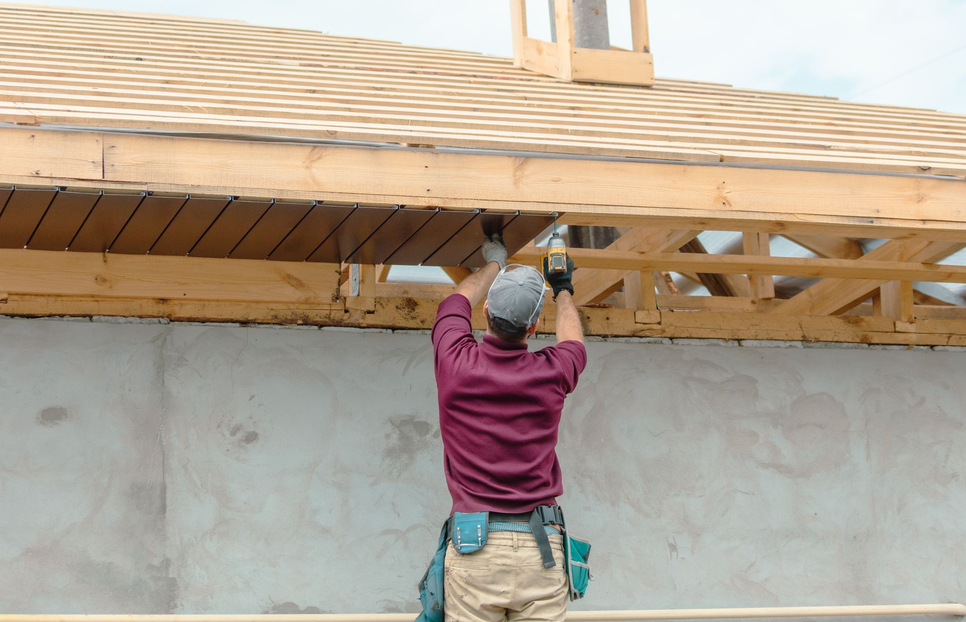 Construction worker on a ladder installing wood paneling under a roof overhang. Construction worker on a ladder installing wood paneling under a roof overhang.