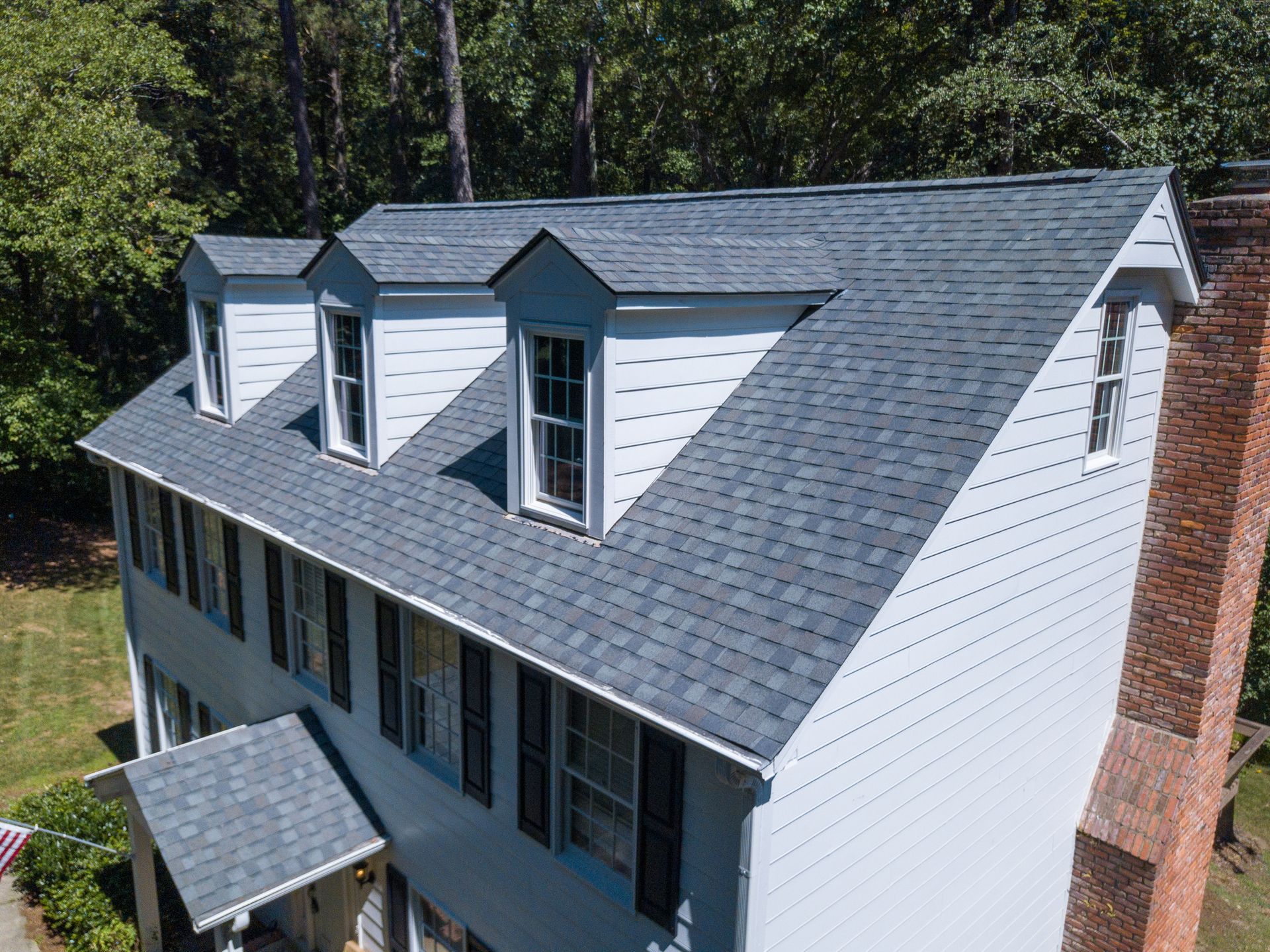 Two-story house with a gray shingle roof, three dormers, and a brick chimney. Two-story house with a gray shingle roof, three dormers, and a brick chimney.