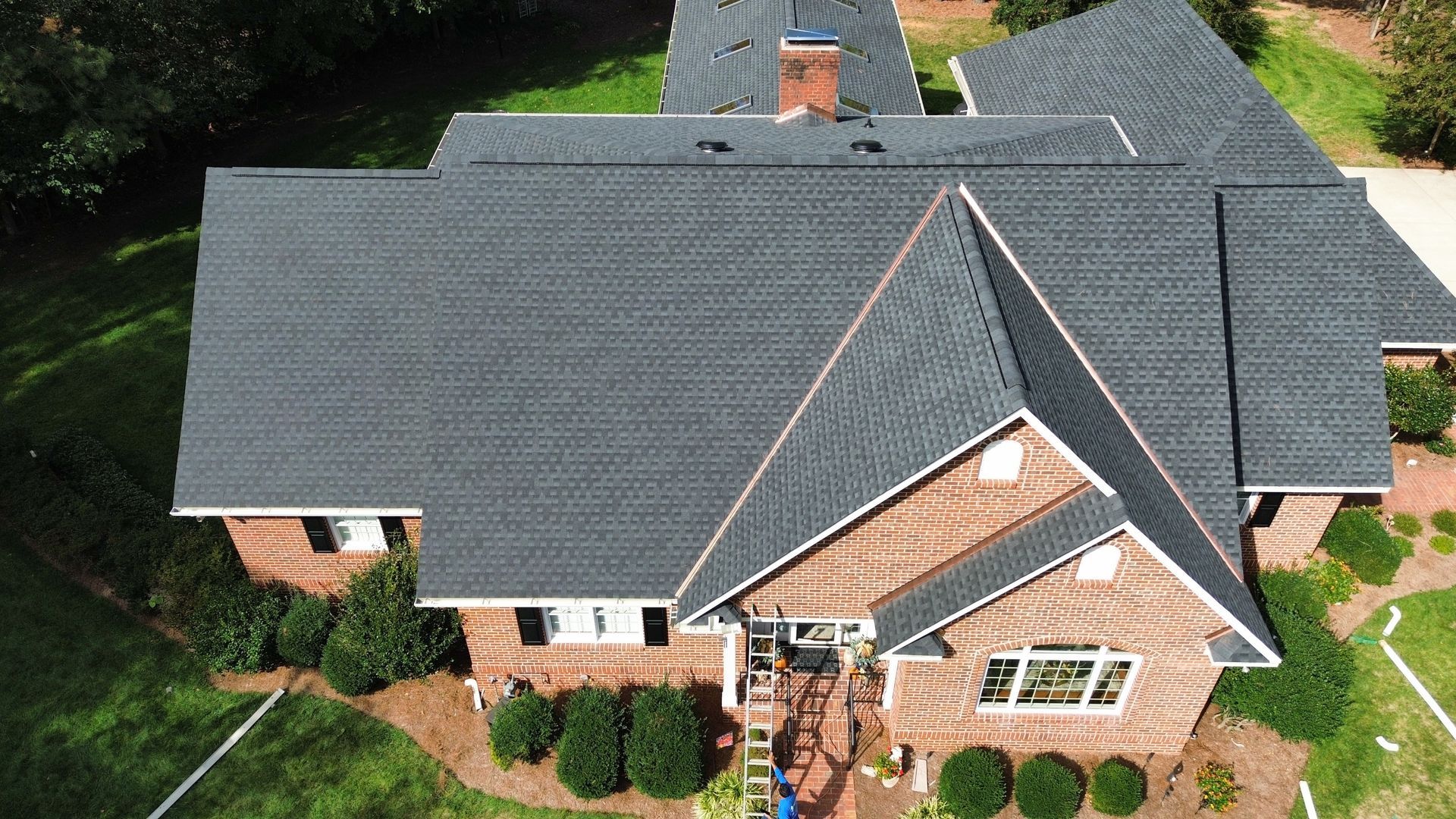 A house with a dark gray shingled roof, brown brick exterior, and green lawn. A house with a dark gray shingled roof, brown brick exterior, and green lawn.