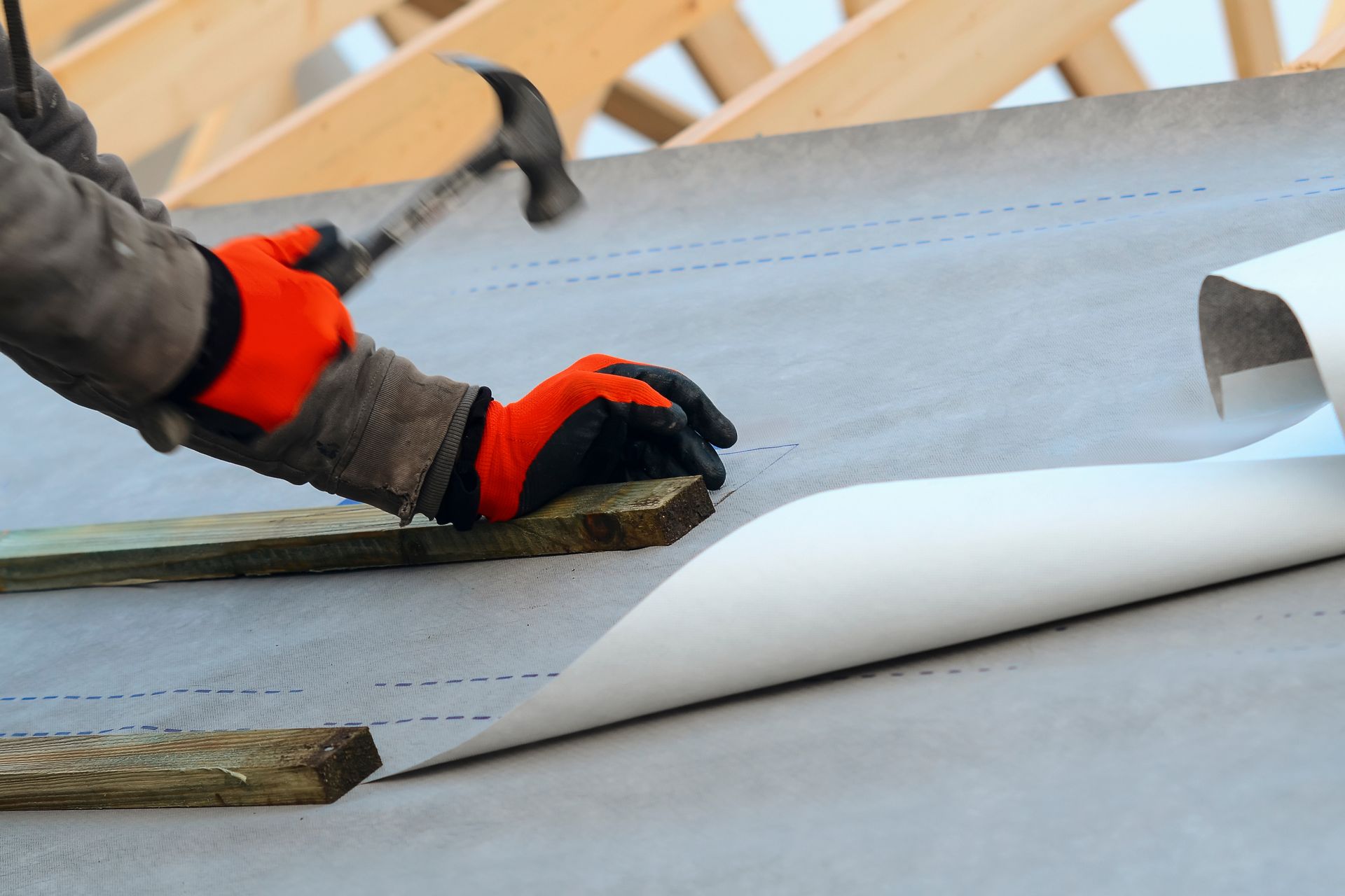Person hammering wood on a roof, wearing orange gloves. Person hammering wood on a roof, wearing orange gloves.