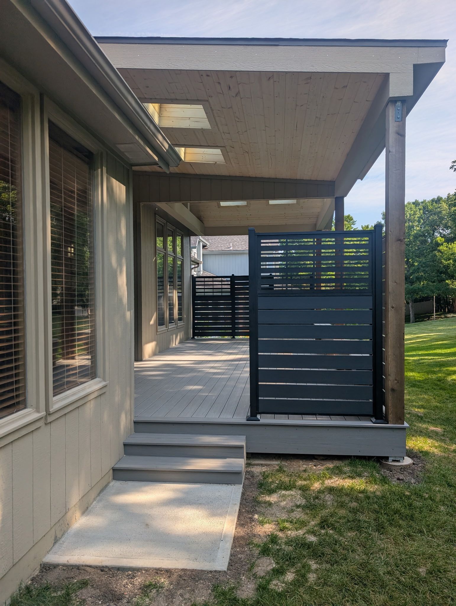 Exterior view of a covered patio with steps, gray deck, and a modern black privacy screen.