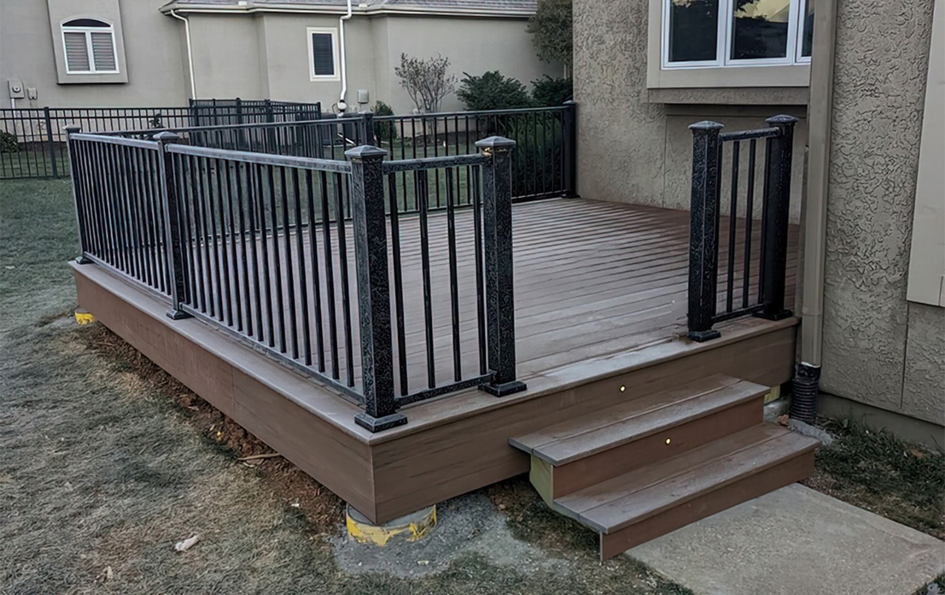 A wooden deck with stairs and a metal railing in front of a house.