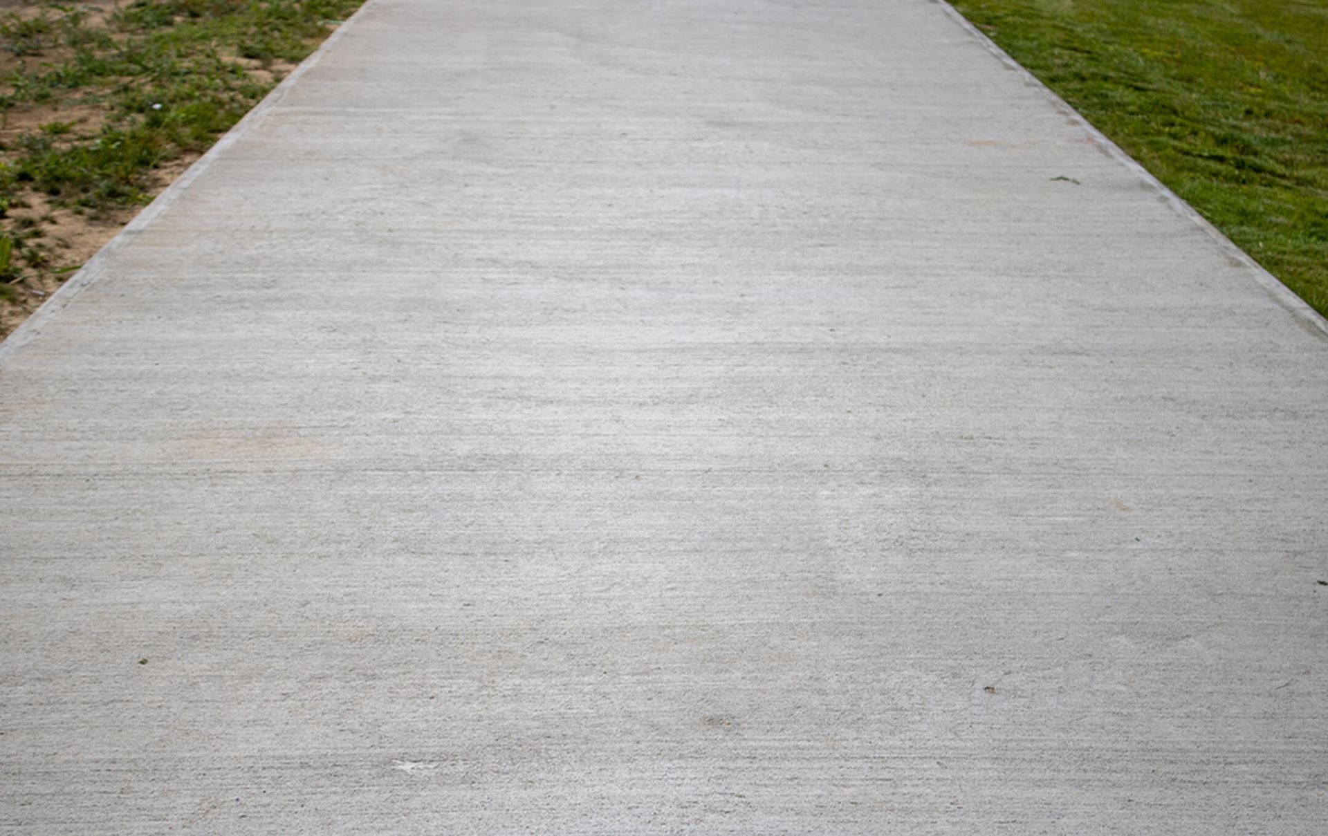 A concrete walkway going through a grassy field.