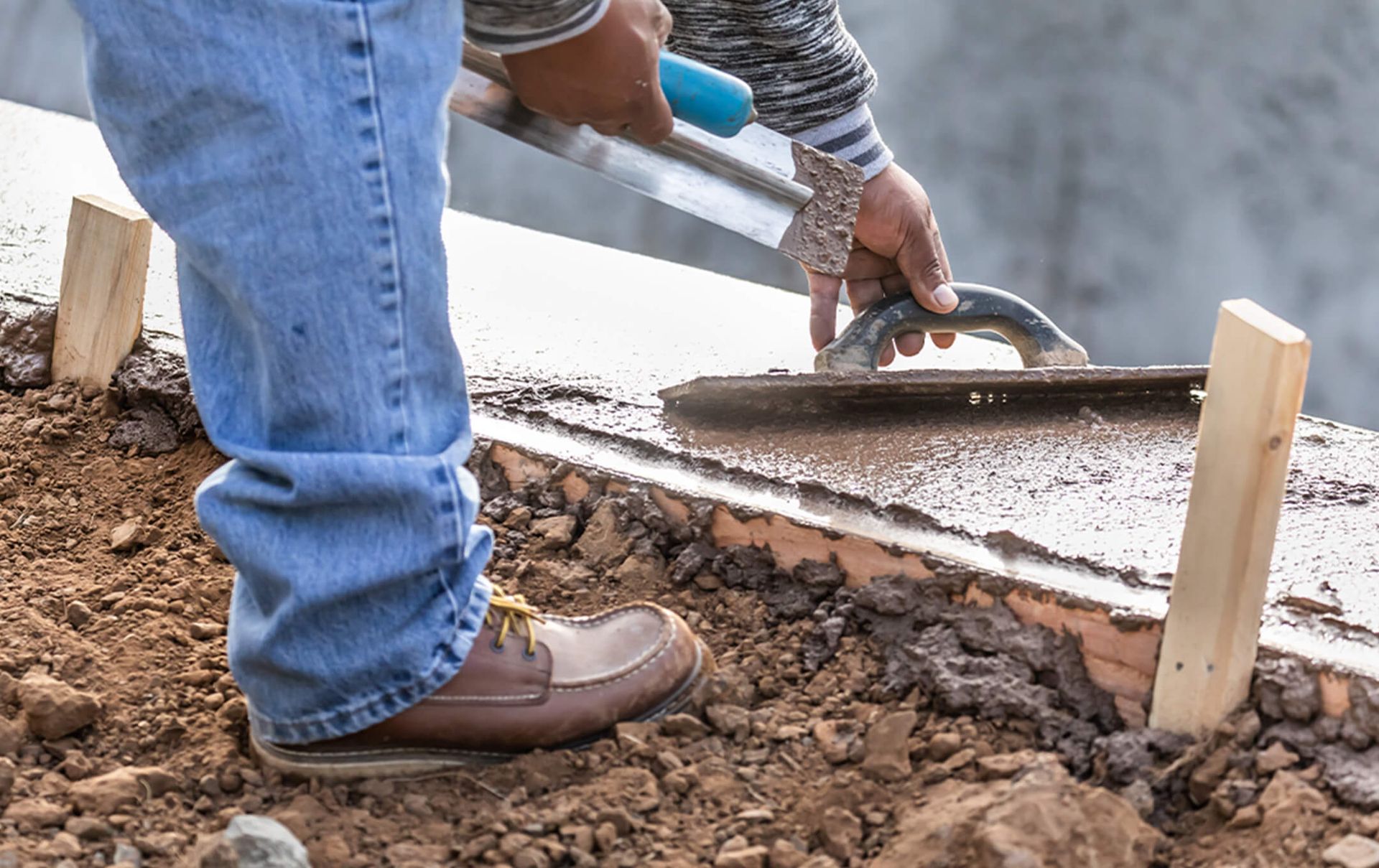 A man is using a trowel to spread concrete on a sidewalk.