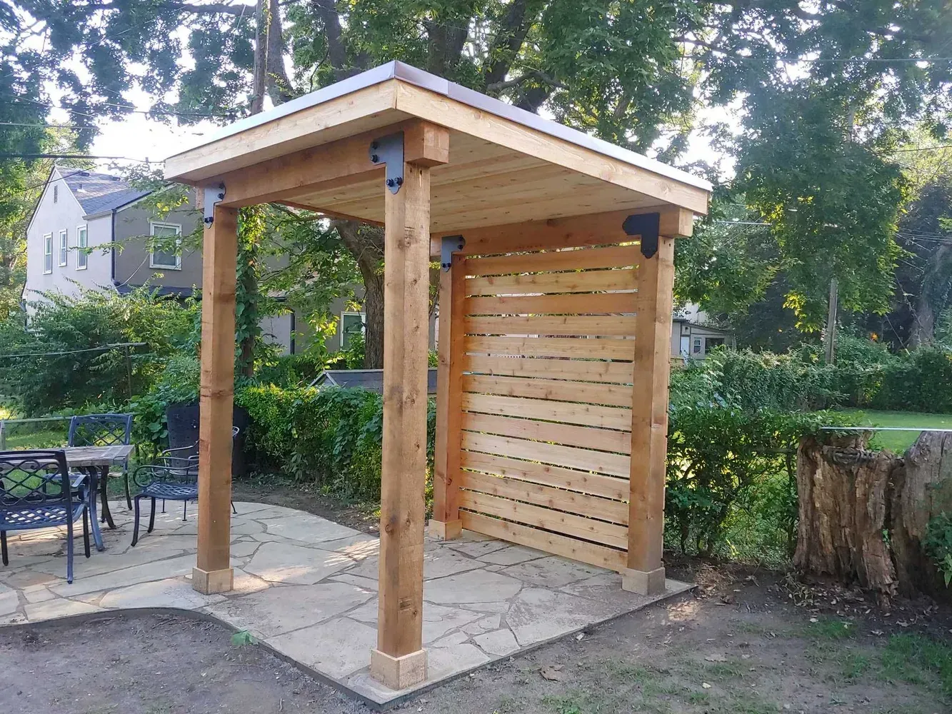 A wooden gazebo is sitting on top of a stone patio in a backyard.