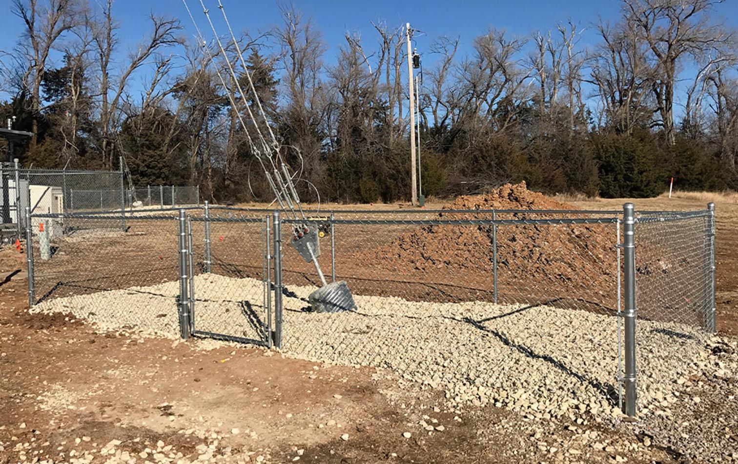 A chain link fence is surrounding a gravel area in a field.