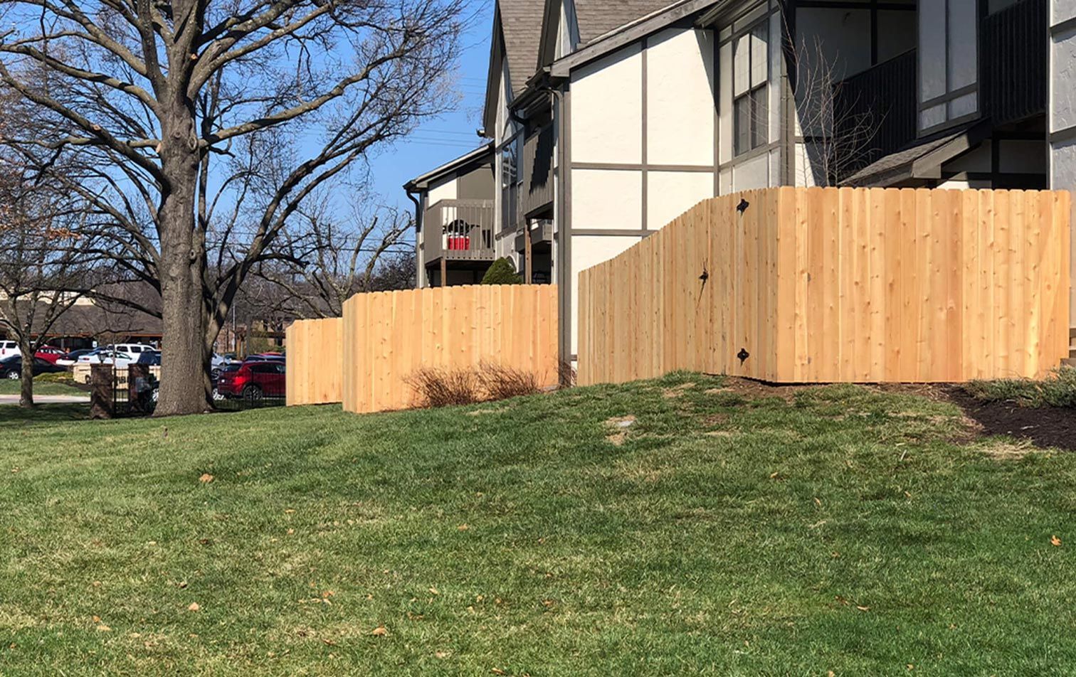 A wooden fence surrounds a lush green lawn in front of a house.